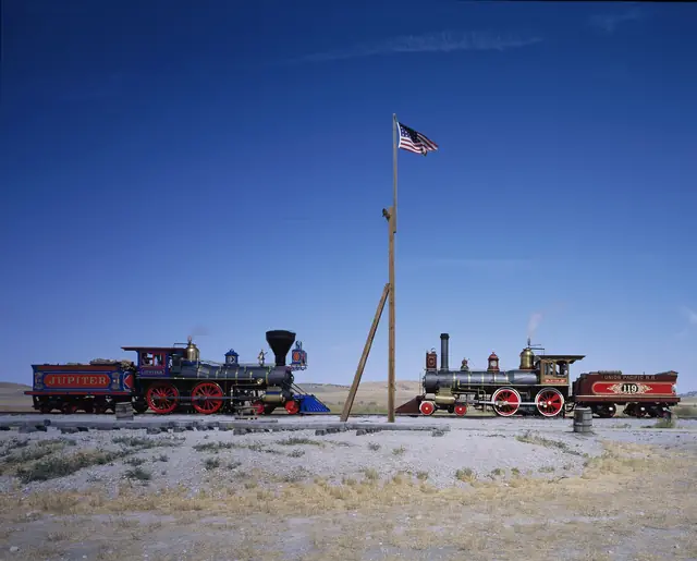 The Jupiter and No. 119 replica locomotives on the tracks at Promontory Summit under a flag and blue sky